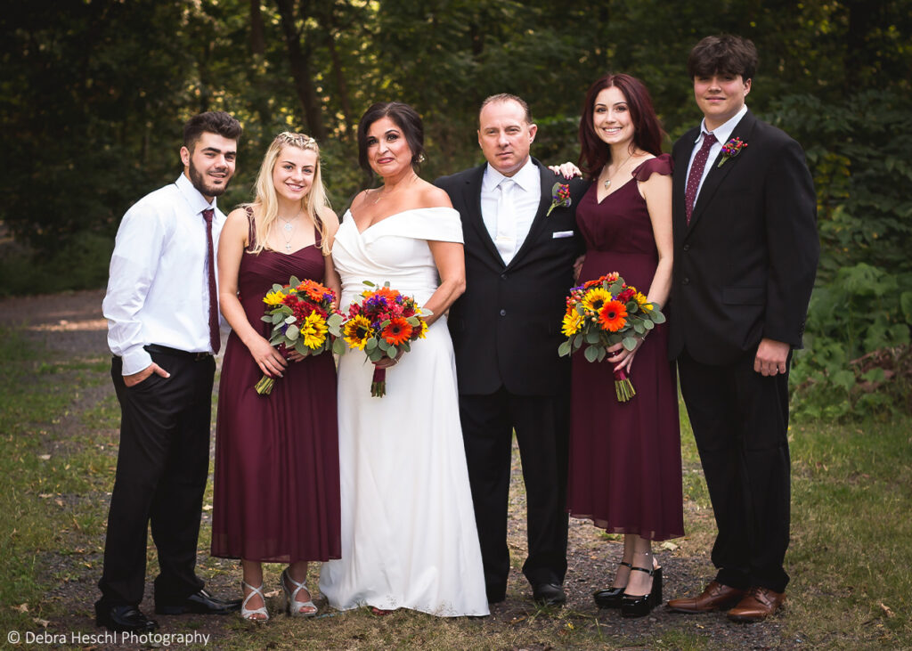 Bride and groom with bridal party in burgundy dresses holding sunflower bouquets on a wooded path at Cutillo's Restaurant wedding