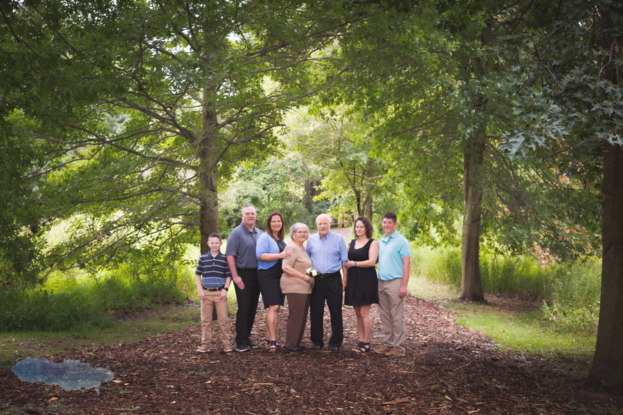 Extended family group portrait under a canopy of trees on a wooded path, taken during an anniversary celebration session in Blue Bell, PA.