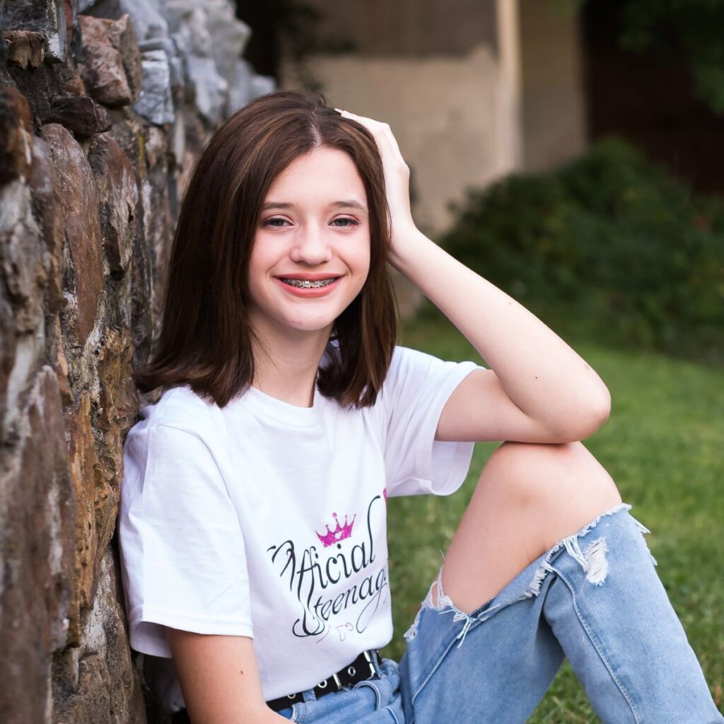 Close-up portrait of smiling 13-year-old girl in Official Teenager shirt leaning against stone wall for birthday photos in Bridgeport PA