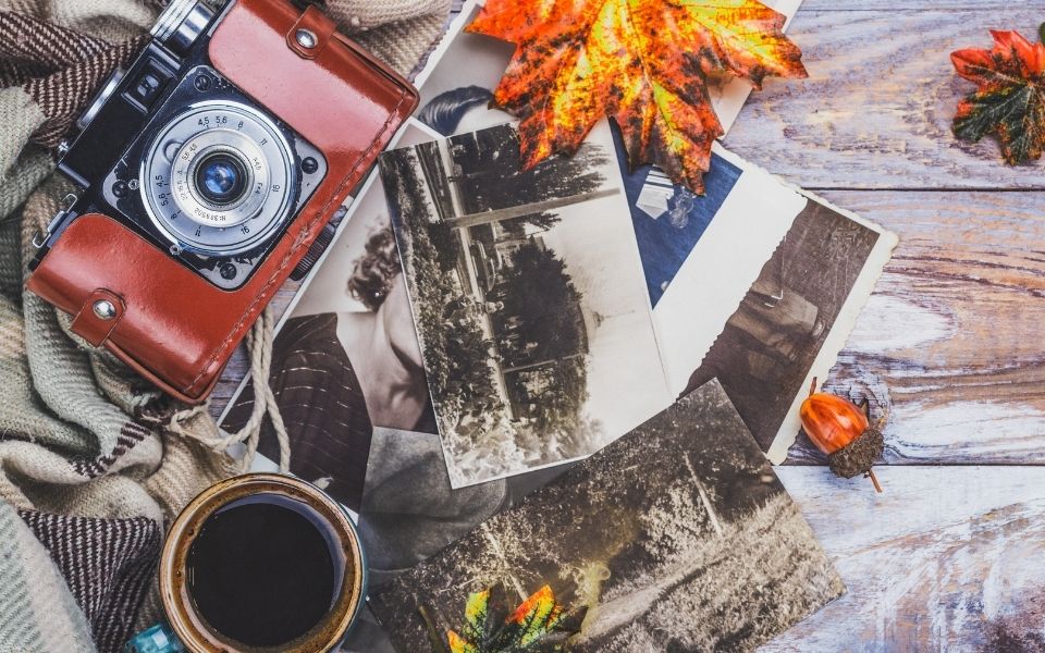 vintage camera, old photographs & coffee mug on table with some fall leaves