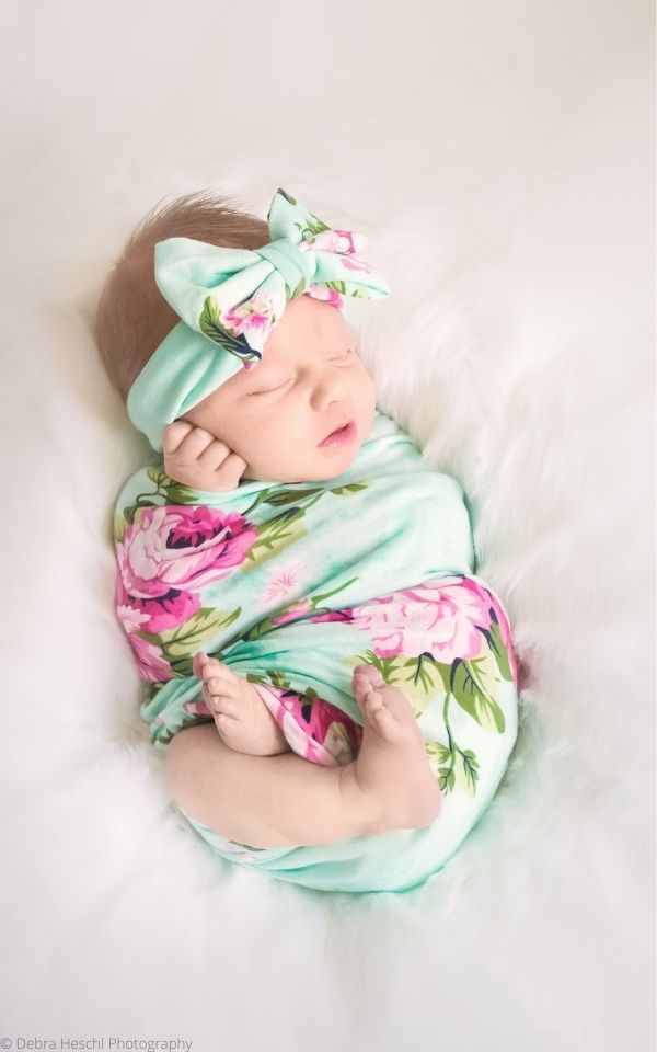 Newborn baby girl wrapped in a flowered blanket wearing a matching headband.