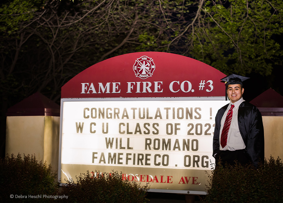 Will-West Chester University Graduate in front of a lit sign for Fame Fire Co. #3 on Rosedale Ave, West Chester, Pa