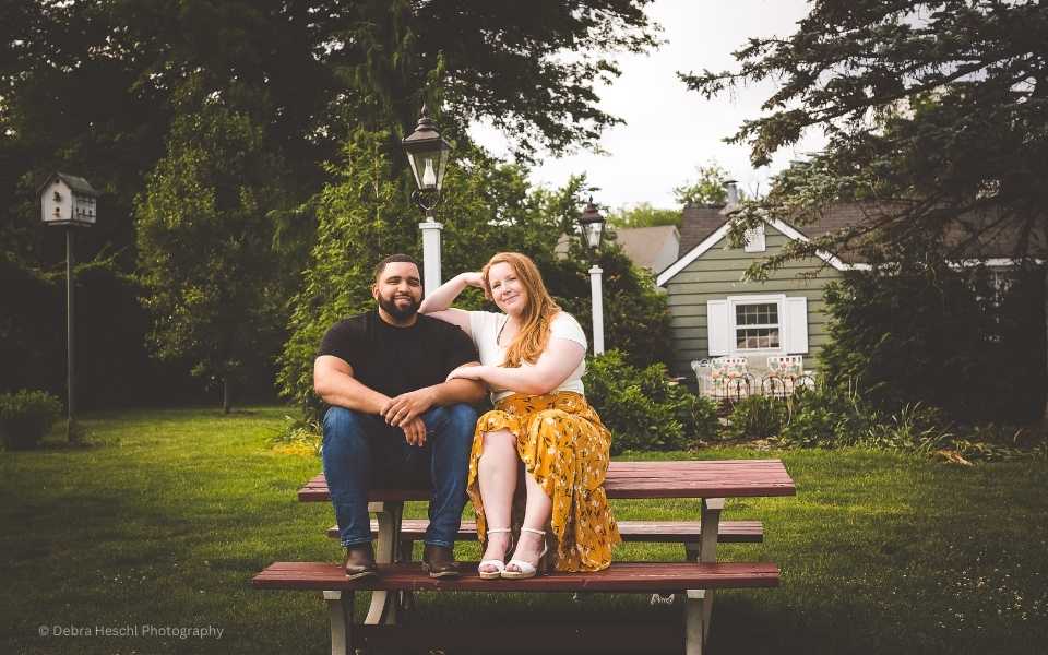 Engaged couple sitting on a picnic table posing a photo at Maple Acres Farm.