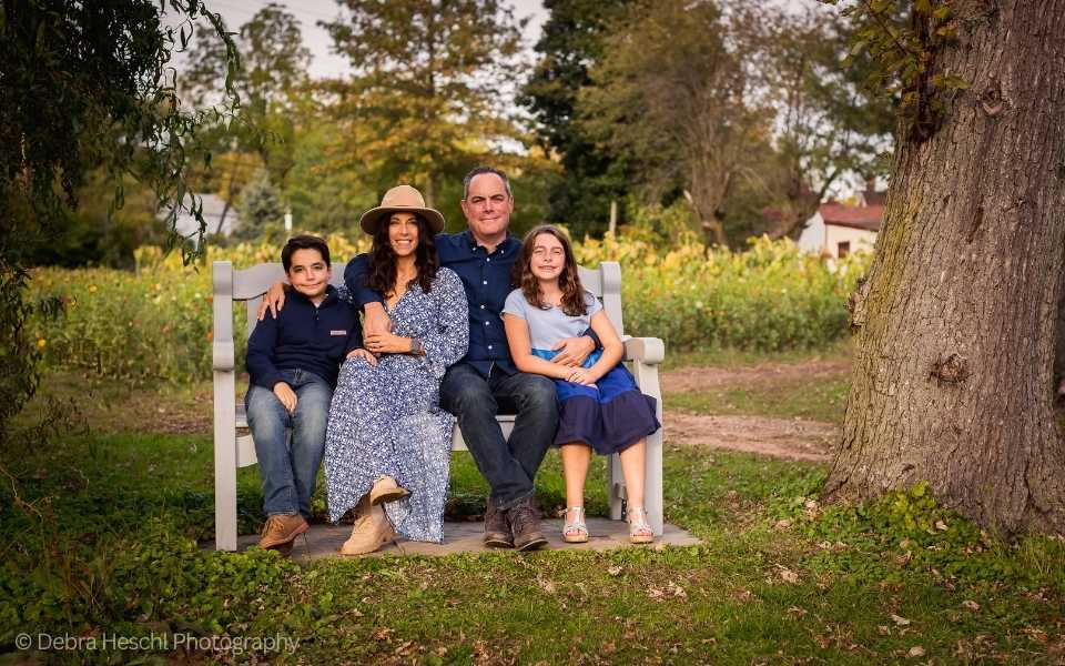 A family of four sitting on a bench for a family photo at Maple Acres Farm in Plymouth Meeting, Pa on a beautiful Fall day.