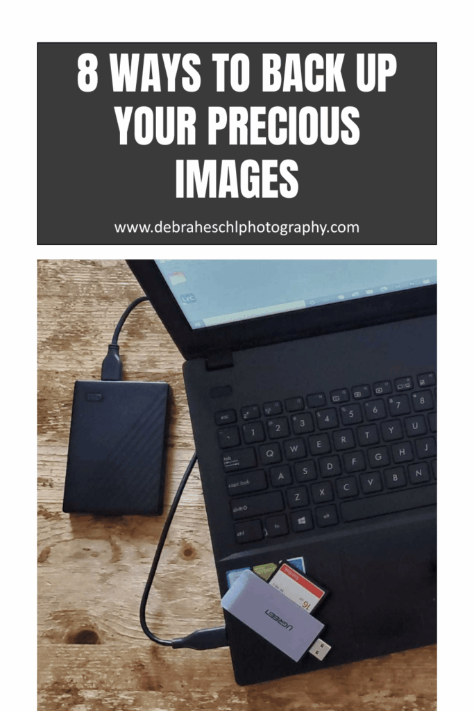 A laptop on a wooden table with an external hard drive connected. Multiple memory cards and a USB hub are nearby. Text reads "8 Ways to Back Up Your Precious Images."