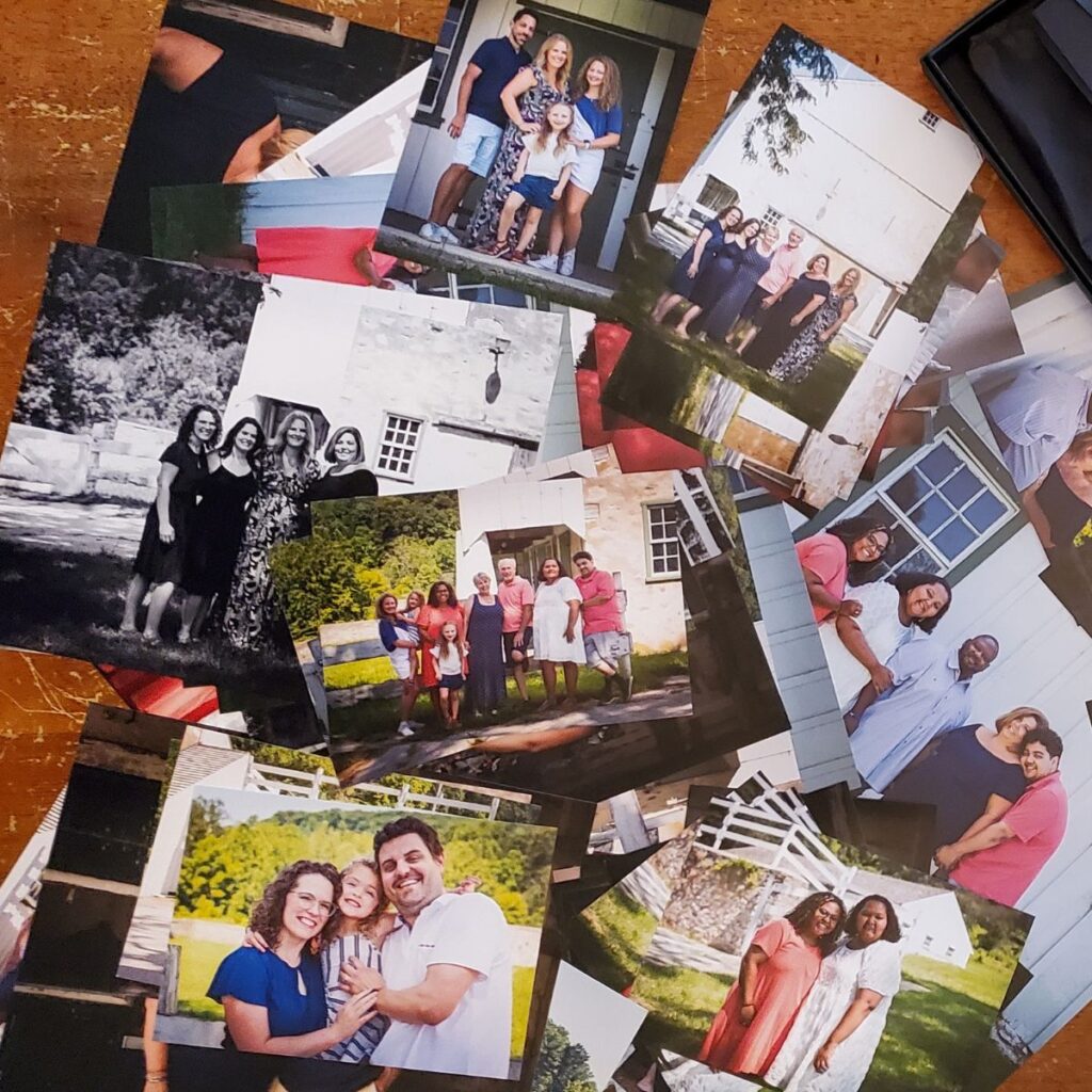 A collection of family photos scattered on a wooden table, showing diverse groups smiling outdoors, conveying warmth and joy in various settings.