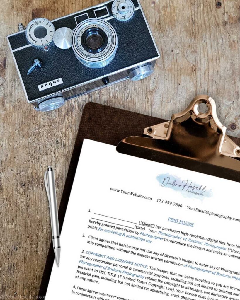 A vintage camera rests on a wooden surface beside a clipboard holding a print release form labeled "Debra Heasch Photography." A pen lies nearby.