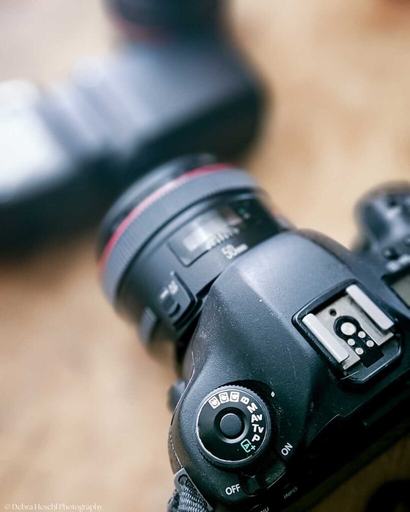 Close-up of a Canon camera's screen showing settings: Manual mode, 1/125 shutter speed, f/2.0 aperture, ISO 1600. A blurred lens appears in the background.