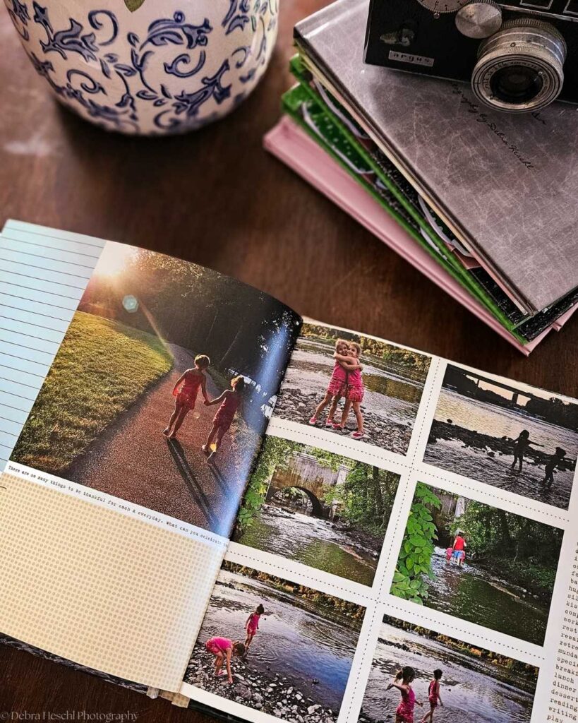An open photo album shows children playing outdoors, evoking joy and nostalgia. A vintage camera and floral vase sit nearby on a wooden table.