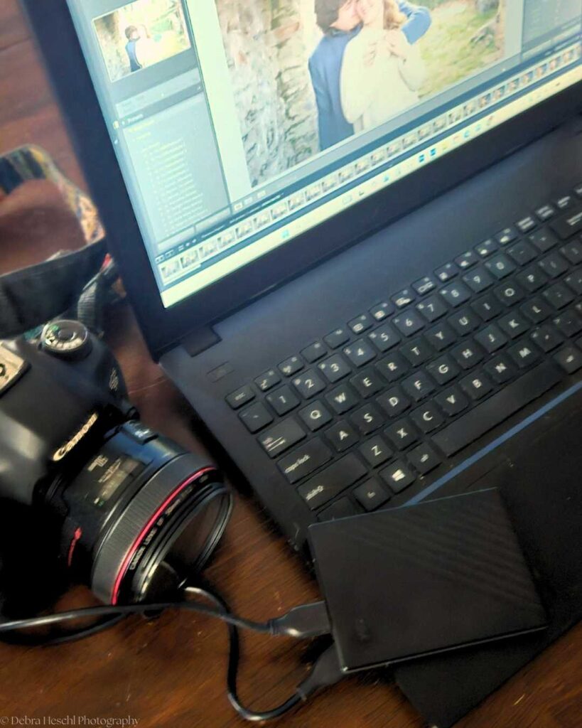 A laptop displays a photo editing program with an image of a couple. A DSLR camera and an external hard drive are connected, suggesting a photography workflow.