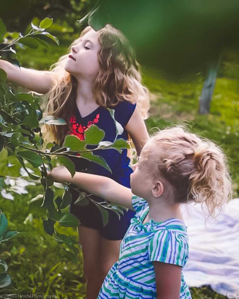 Two young girls exploring leafy branches during a candid outdoor kids photo session.