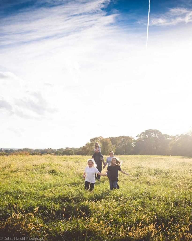 Family of five running through a sunny field during an outdoor kids photo session.