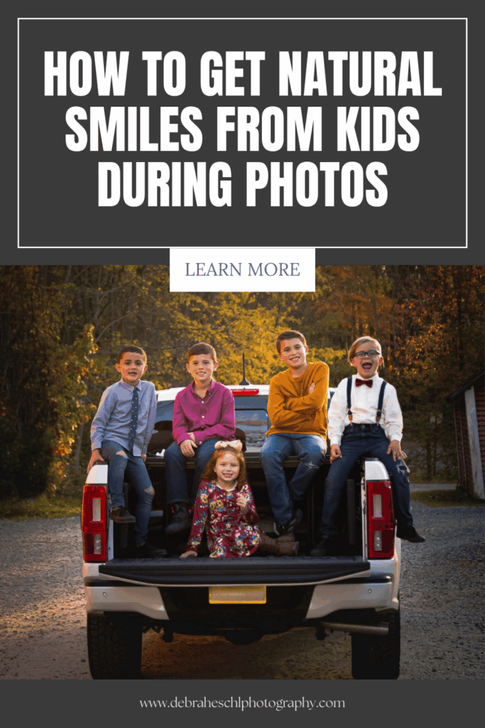 A group of smiling children sits on the open tailgate of a pickup truck surrounded by autumn foliage. Text above reads 'How to Get Natural Smiles from Kids During Photos.' The scene conveys warmth and joy. A website link is provided below.