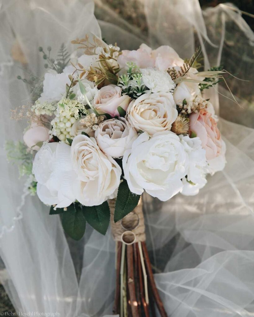Elegant bridal bouquet with pale pink and white roses, wrapped in twine, rests on soft tulle. The arrangement evokes romance and natural beauty.
