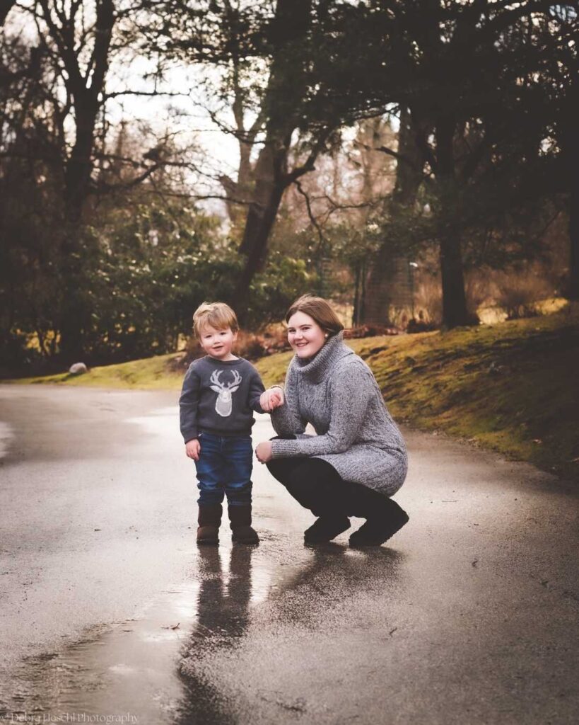 Big sister crouching next to a toddler boy during an outdoor kids photo session on a rainy park path.