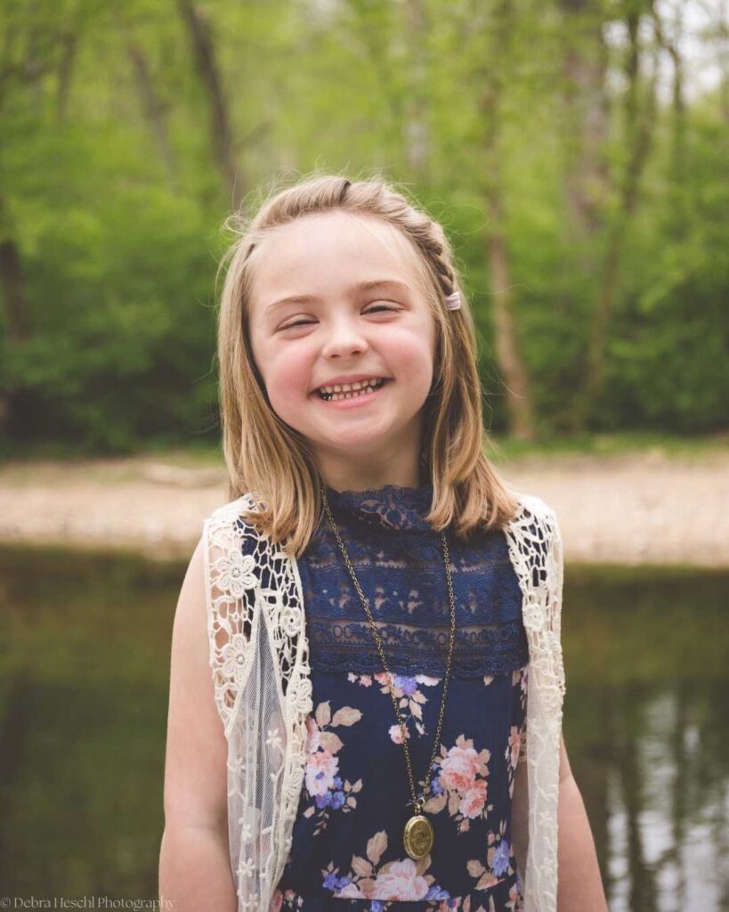 Candid portrait of a young girl laughing naturally during an outdoor photography session by a pond.