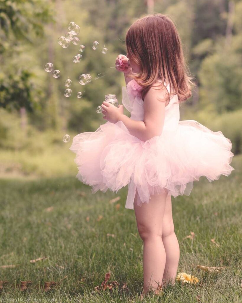 Young girl in a pink tutu blowing bubbles outdoors during a relaxed natural light children's photography session with Debra Heschl Photography