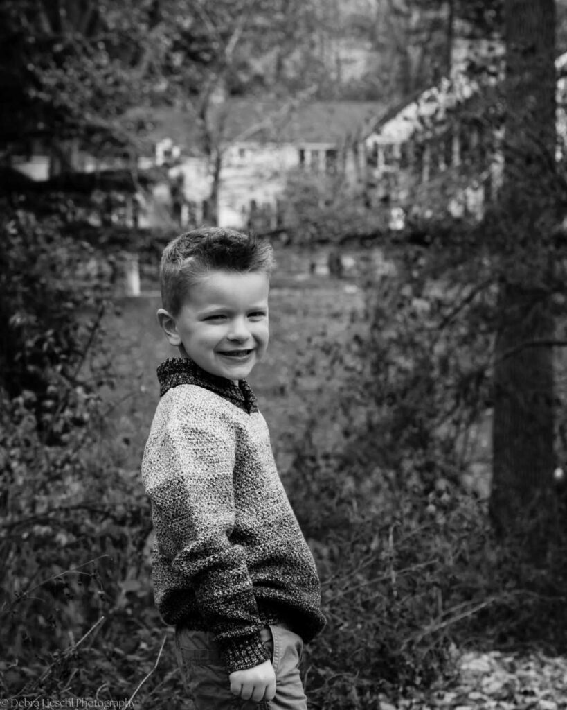 Black and white candid portrait of a young boy looking back over his shoulder with a genuine smile.