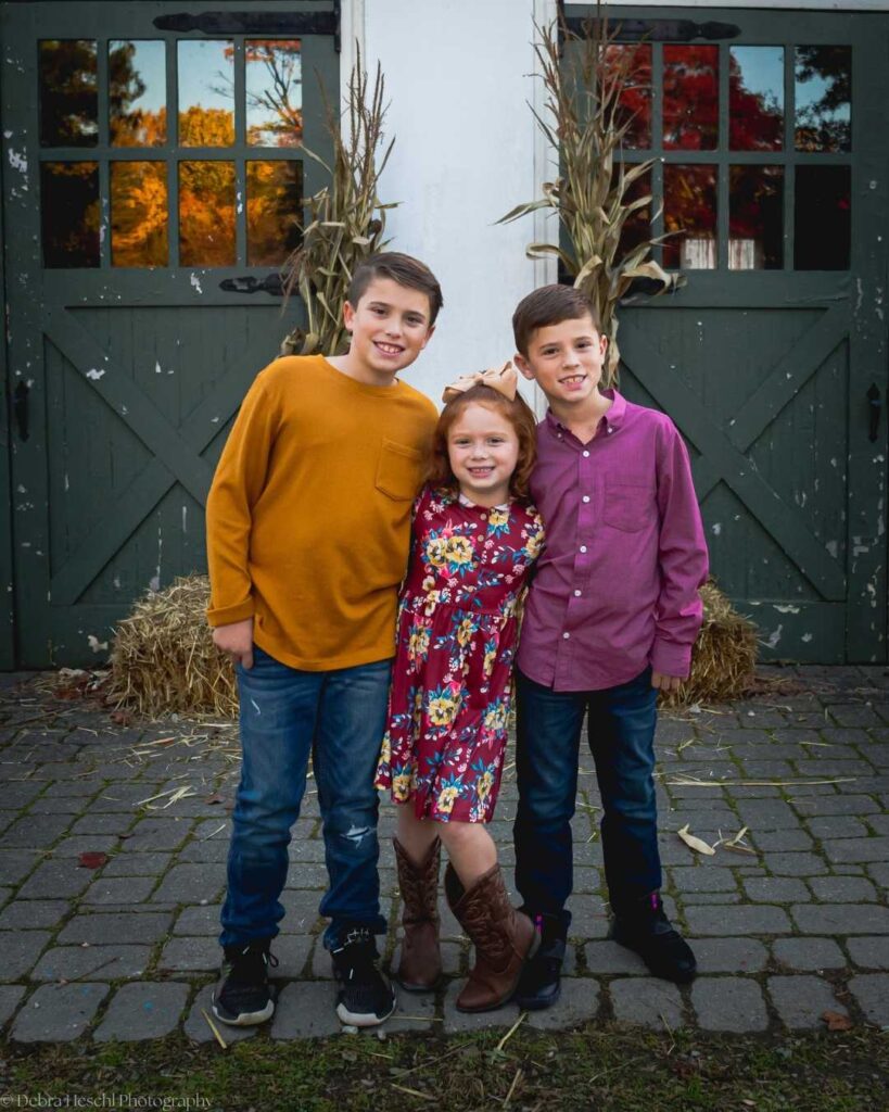 Three siblings posing naturally together in front of a barn during a fall outdoor photography session