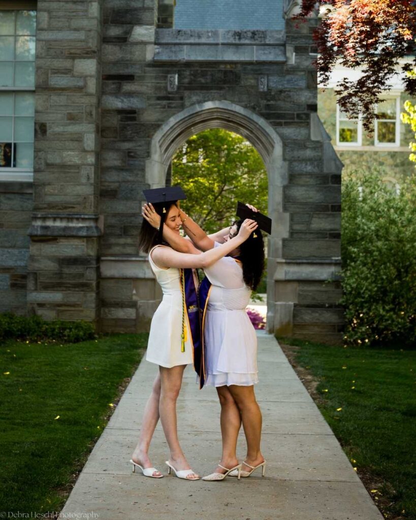 Miranda and Leah, best friends, sharing a sweet graduation cap moment at West Chester University archway