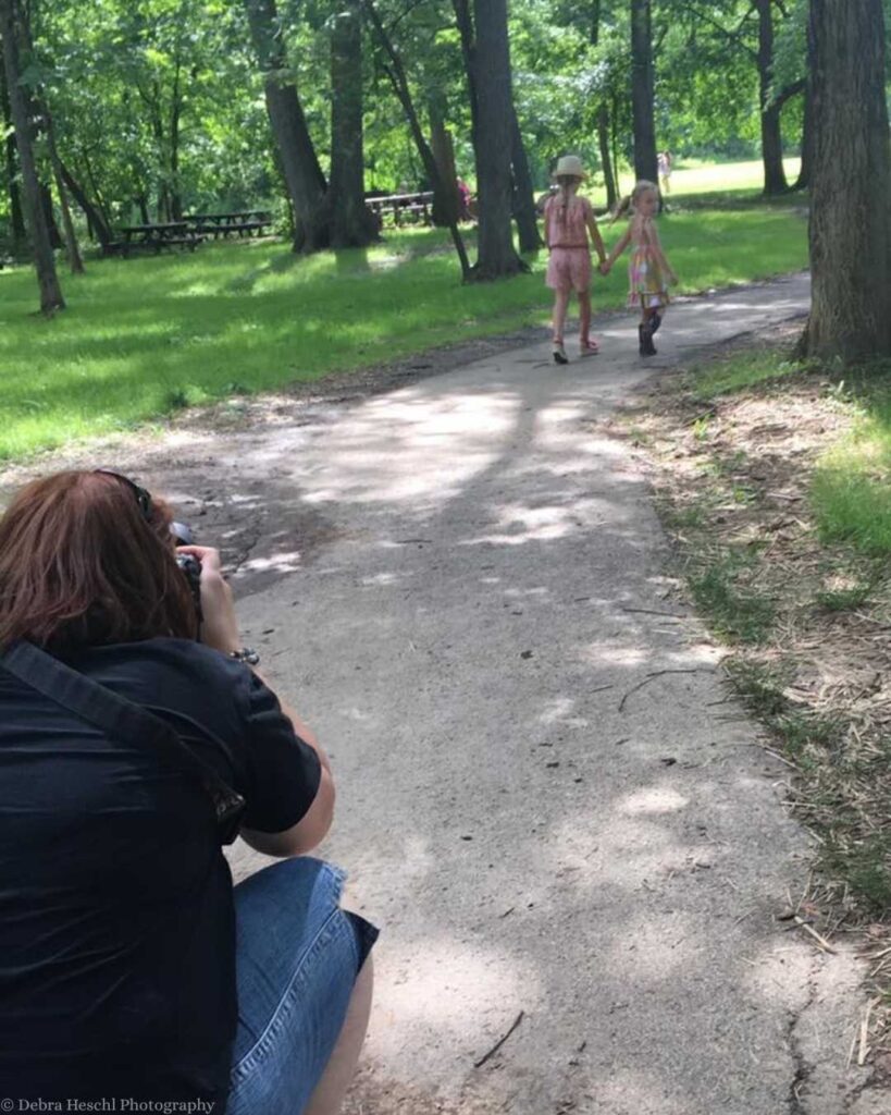 What happens after your photo session starts here: photographer capturing candid moments of two sisters walking outdoors.