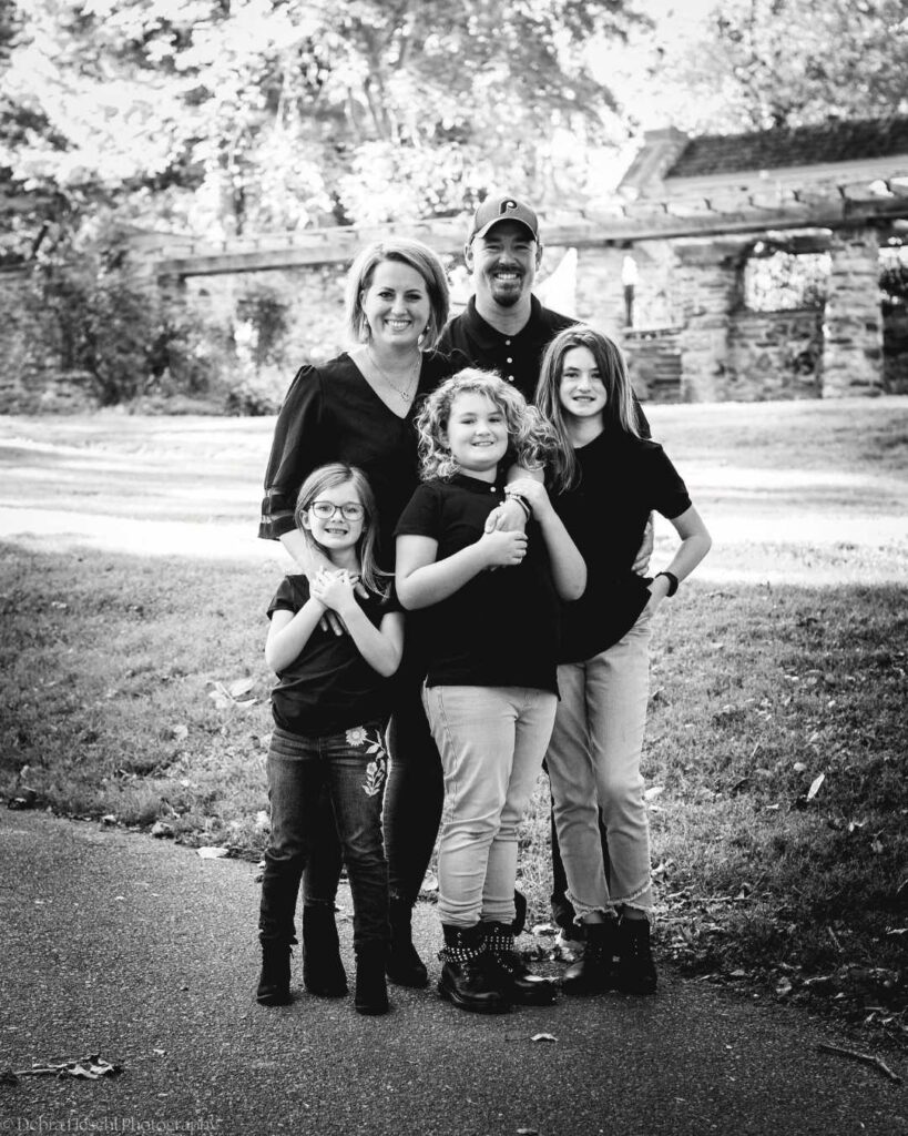 Black-and-white family portrait of parents and three daughters during an outdoor session at Manor House of Prophecy Creek in Blue Bell, PA.