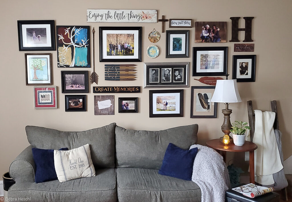 Eclectic gallery wall design above a gray sofa with mixed black frames, family photos, and wooden signs