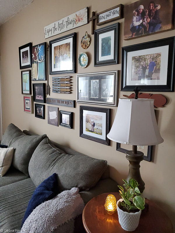 Full gallery wall layout above a gray sofa with vintage lamp, wooden signs, and family photo frames