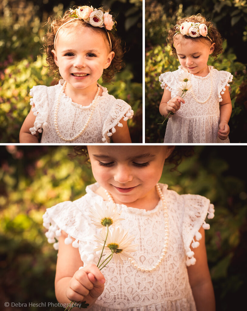 Toddler girl in a floral crown and lace dress with a pearl necklace smiling and holding daisies during a family photography session in Bryn Mawr, PA