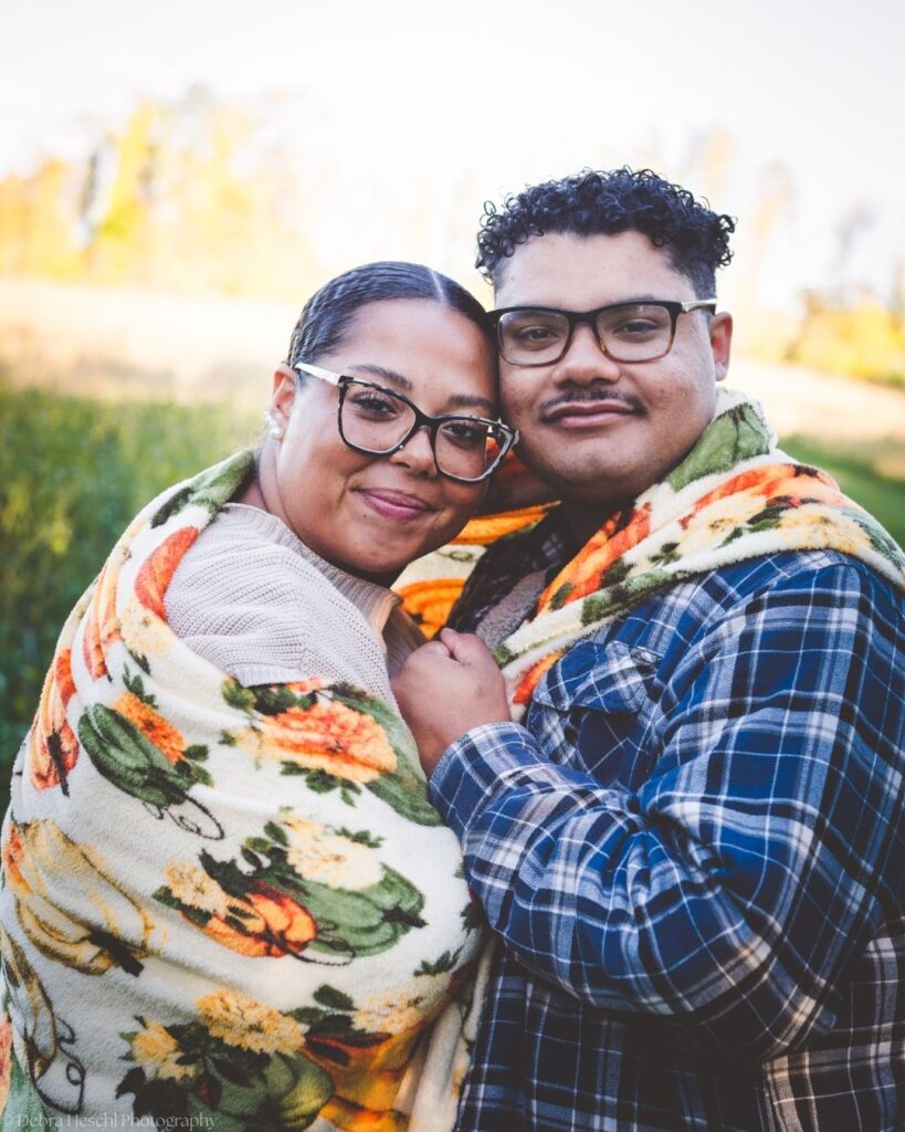 Hannah and Richard cuddled together in a cozy pumpkin-print blanket during their fall photo session at Manor House.